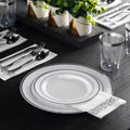 Silver-rim disposable dinnerware with silver-scroll napkin in a table setting; decorative plants not included