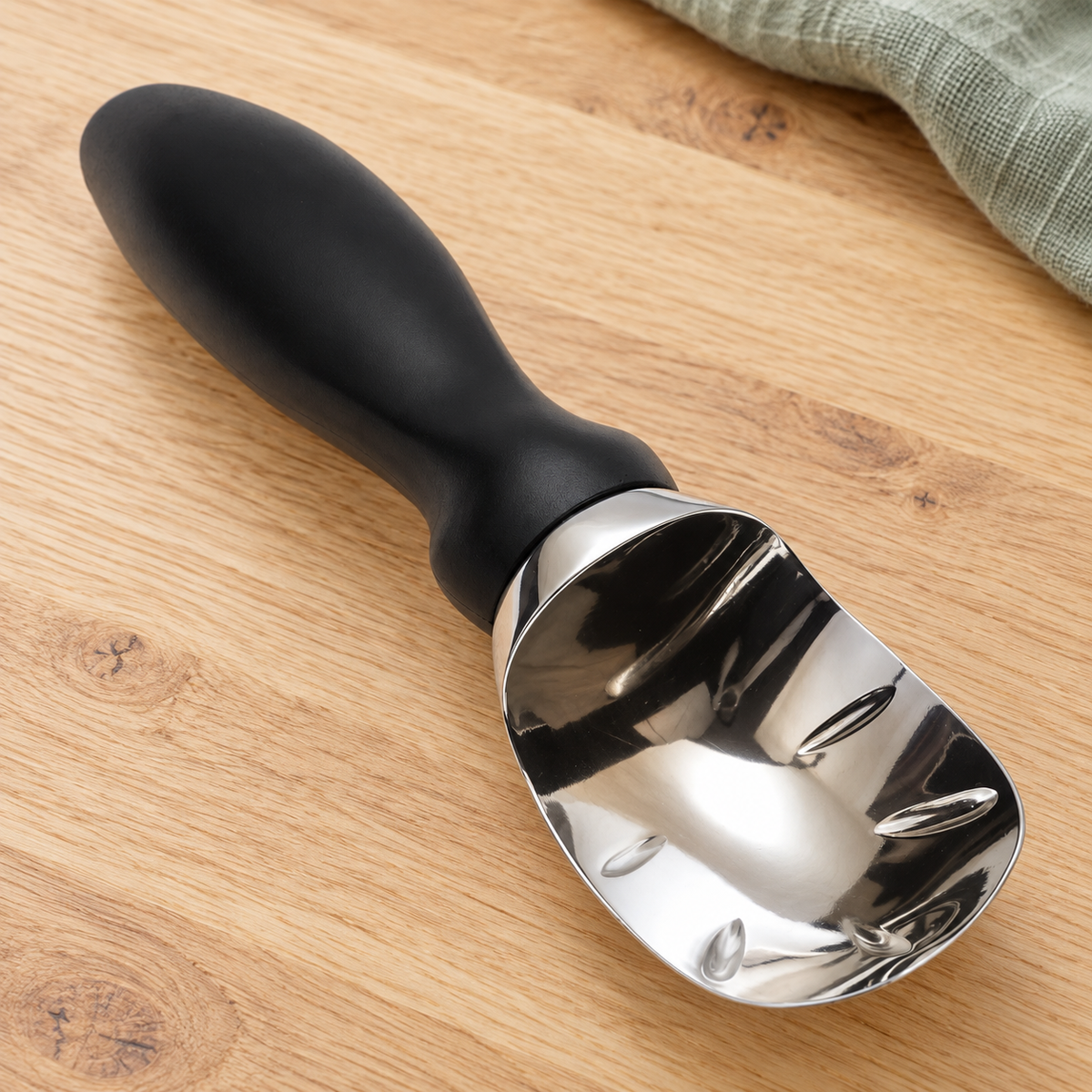 Metal ice cream scoop with black handle on an oak table; linen is a styling prop