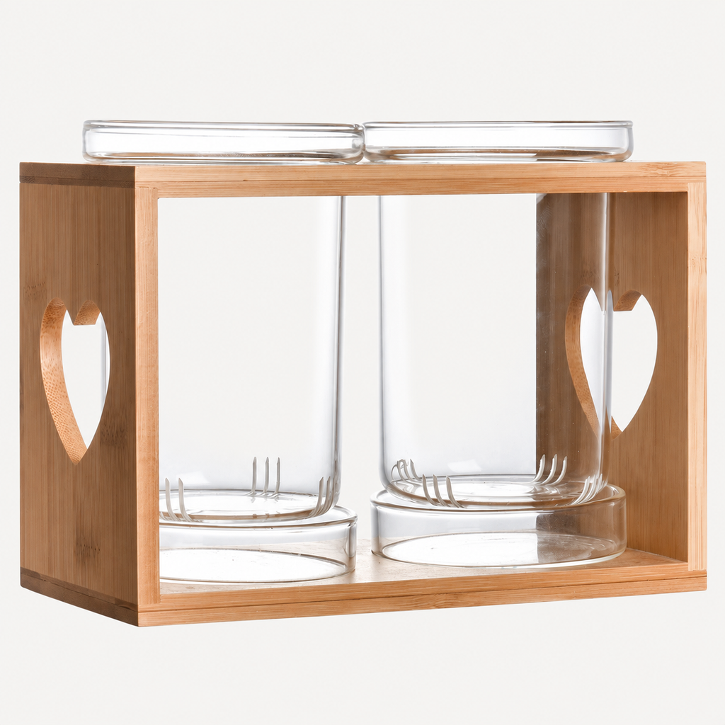 Two empty clear glass draining cups with lower drainage slots and separate catch trays in a wood frame with heart-shaped side cutouts.