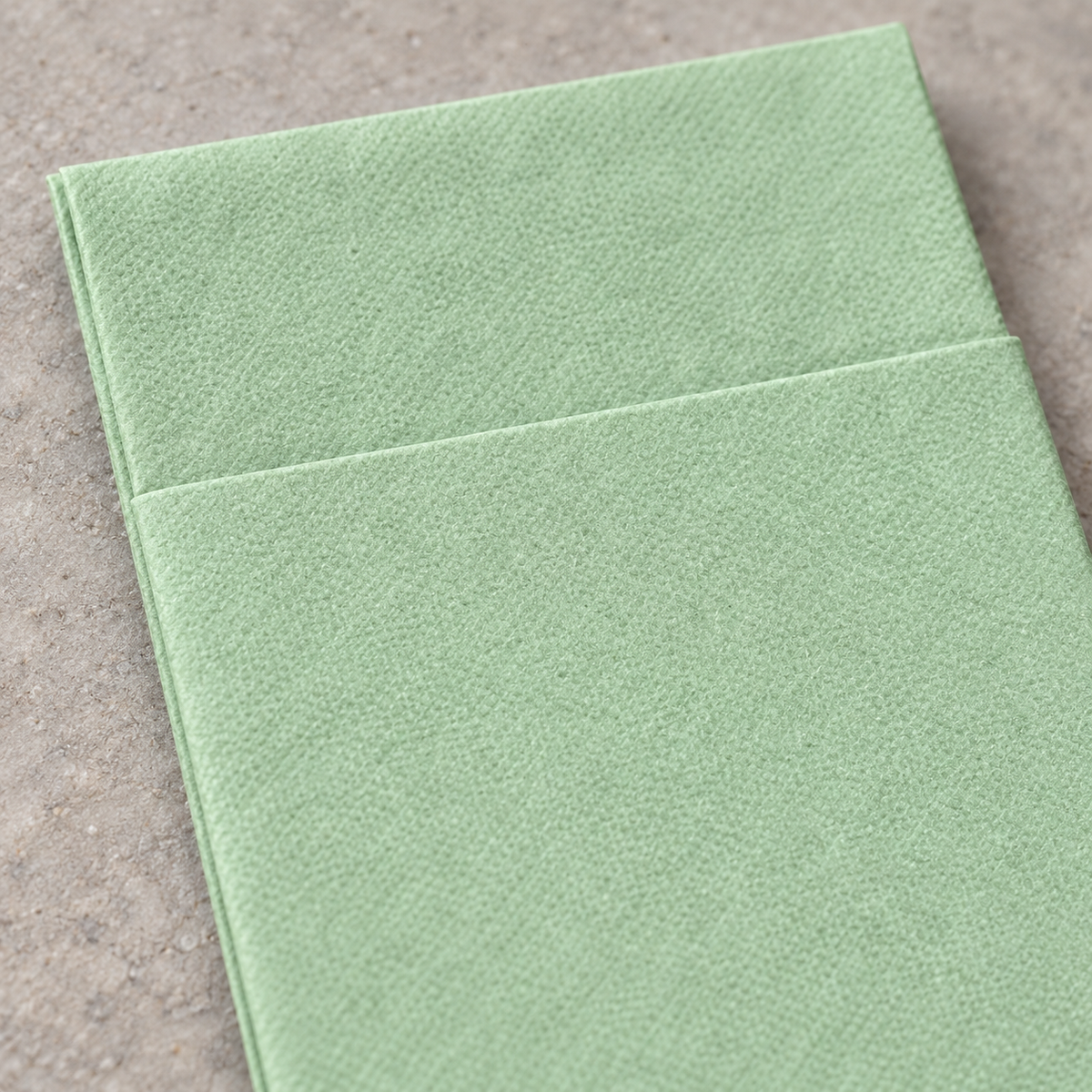 Close-up of the avocado green paper napkin's straight pocket edge and texture.