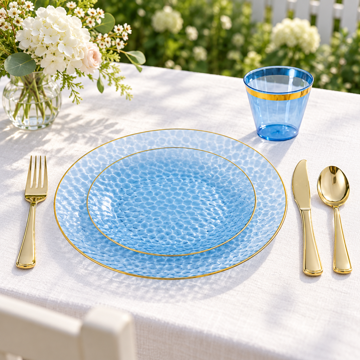 Blue and gold plates, cup and cutlery at an outdoor garden table; decor not included.