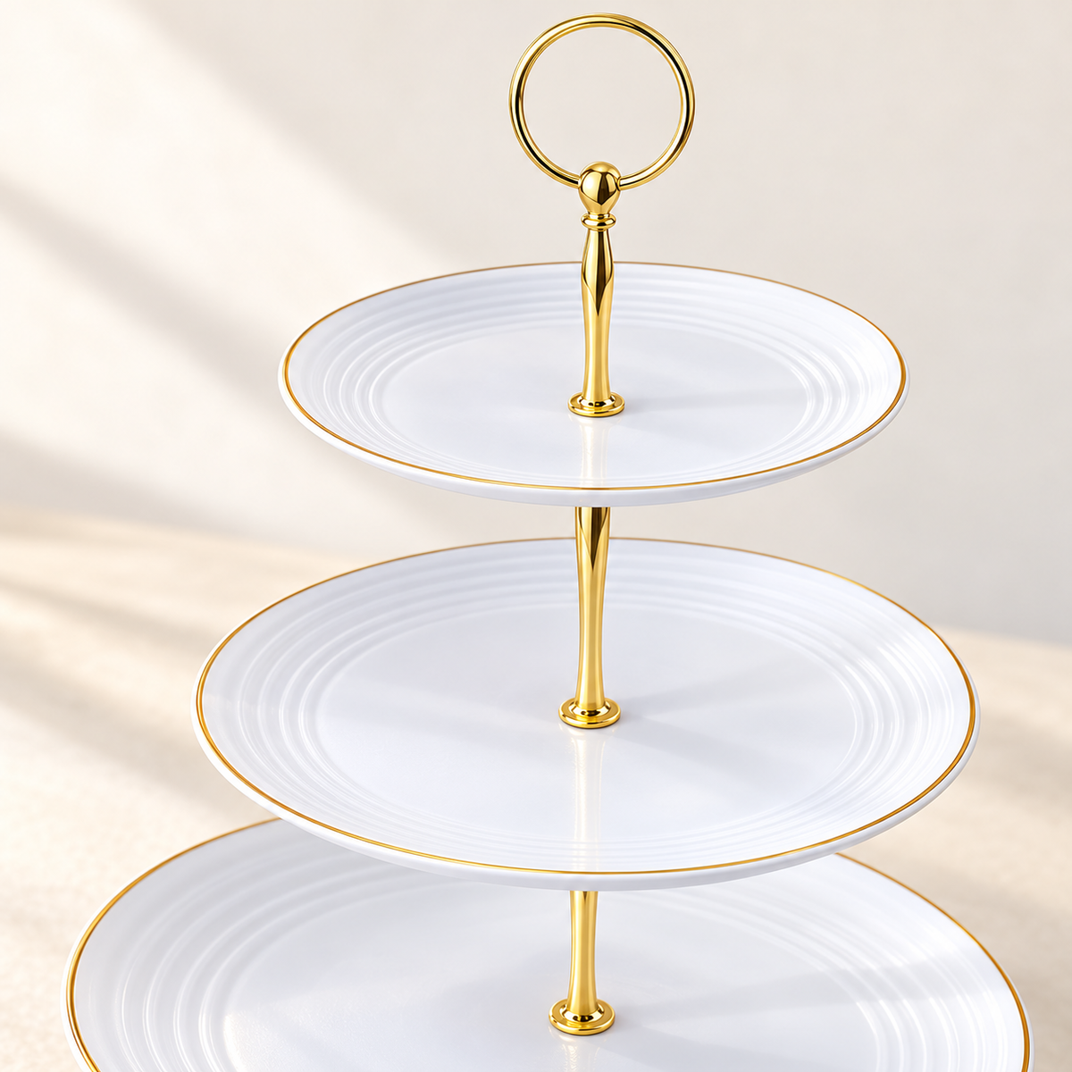 Close-up of the three-tier stand's white molded plates, thin gold-tone rims, ring handle and tapered center posts.