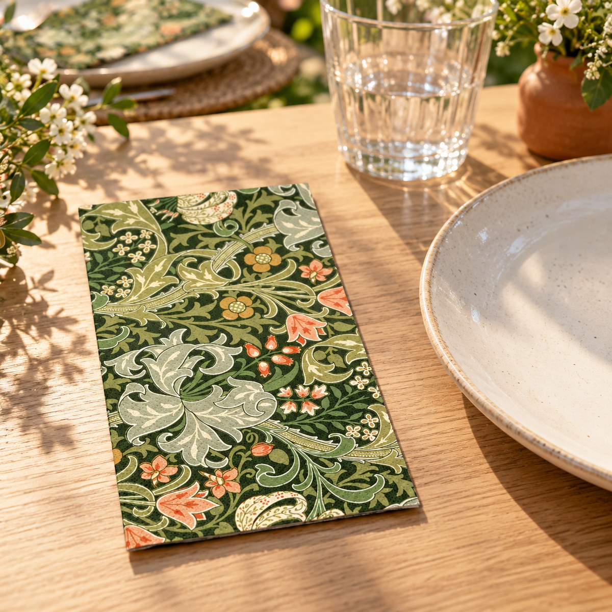 Dark-green botanical paper napkin on a wooden garden table; tableware and styling props not included.