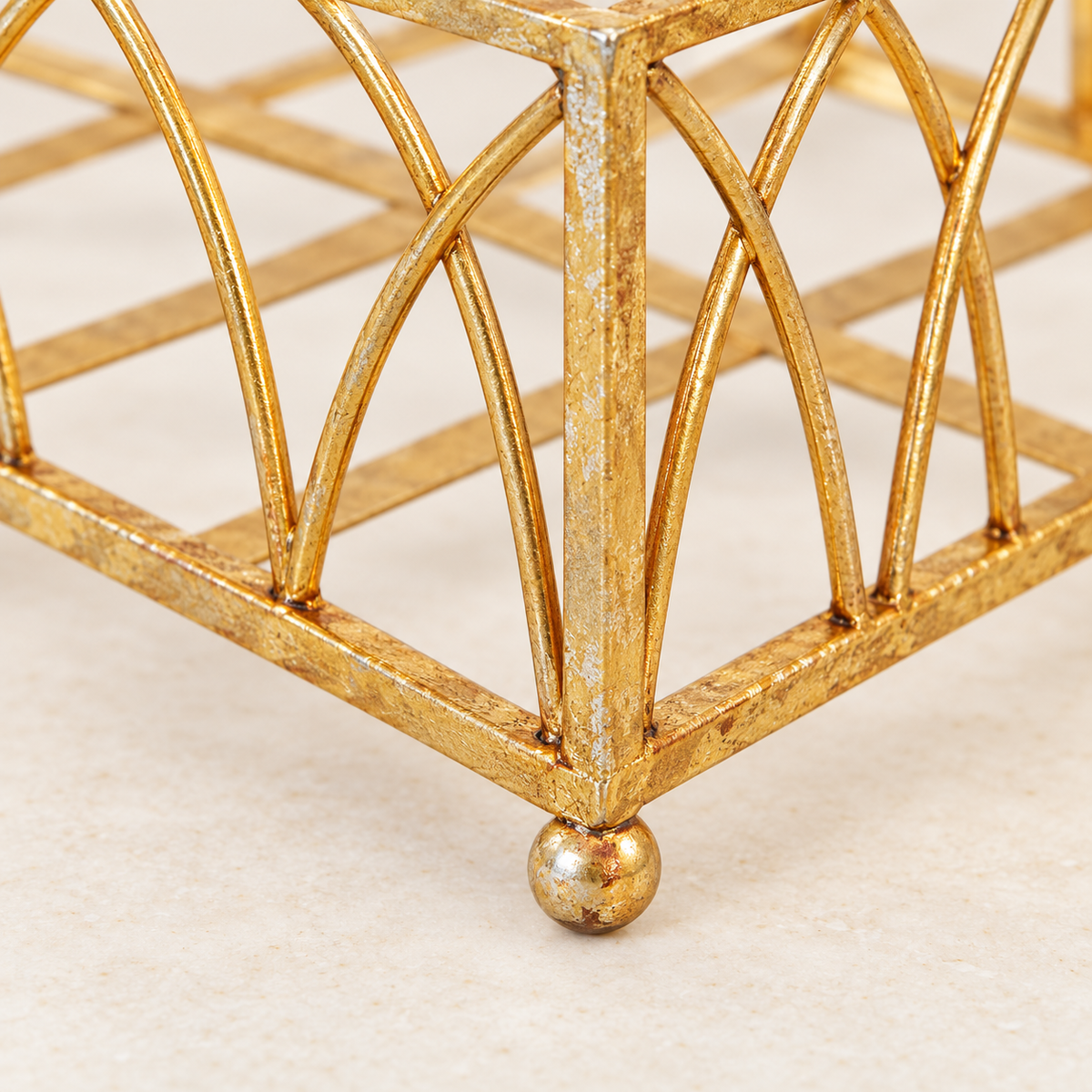 Close-up of a Gold Arch Napkin Caddy ball foot, corner joint and textured gold finish