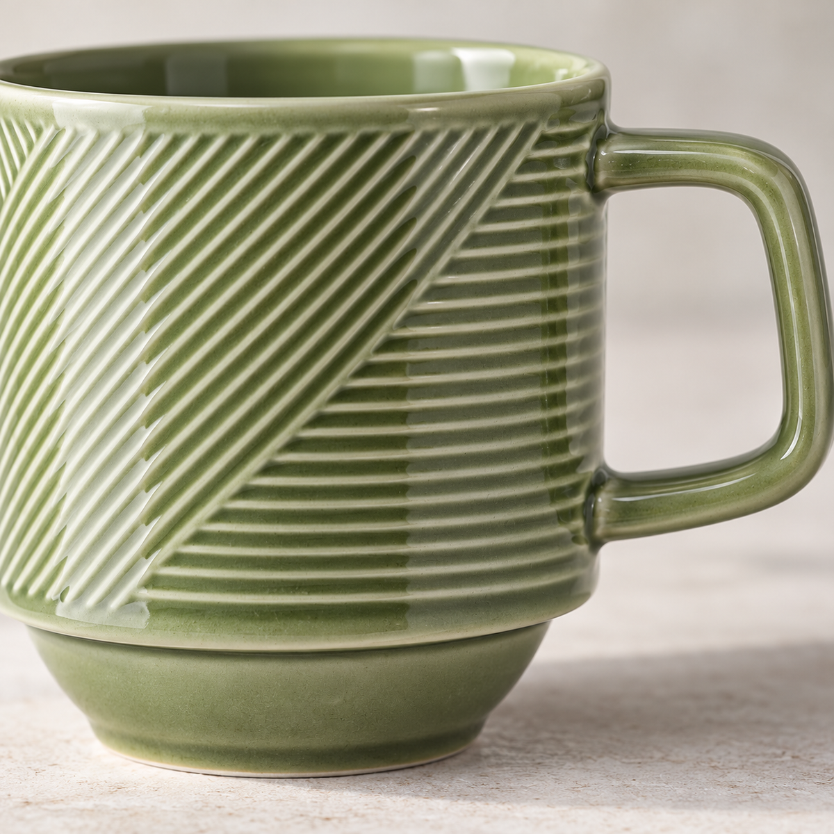 Close-up of the green glazed relief, angular handle and recessed stacking foot of a pea-green ceramic mug.