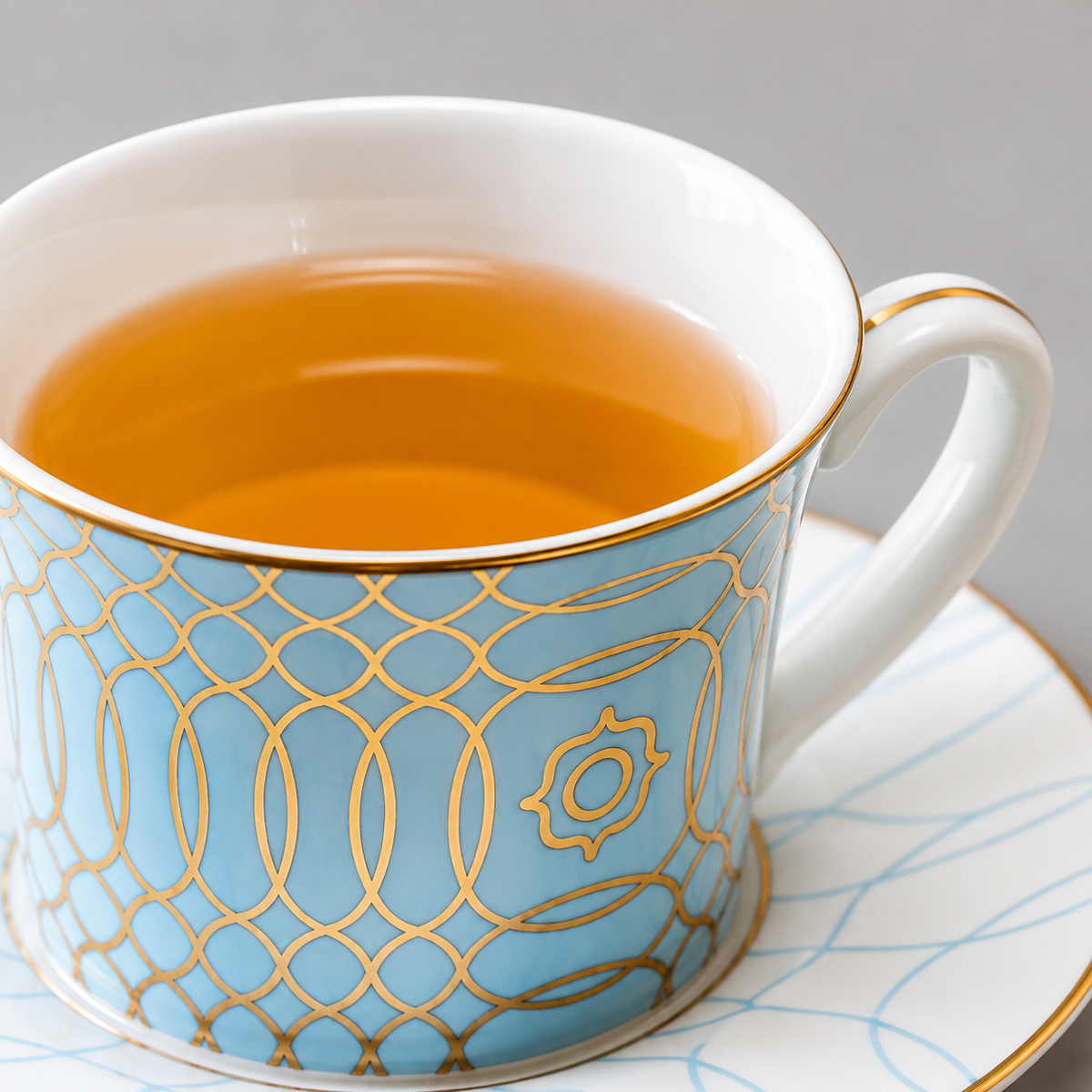 Close-up of the tea cup's white interior, fine gold rim and white handle with gold accent. Tea is a styling prop, not included.