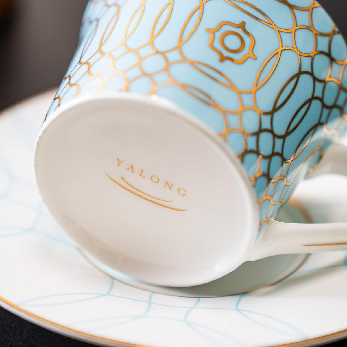Actual supplier photograph of light blue porcelain cup with gold geometric pattern, white handle and maker mark.