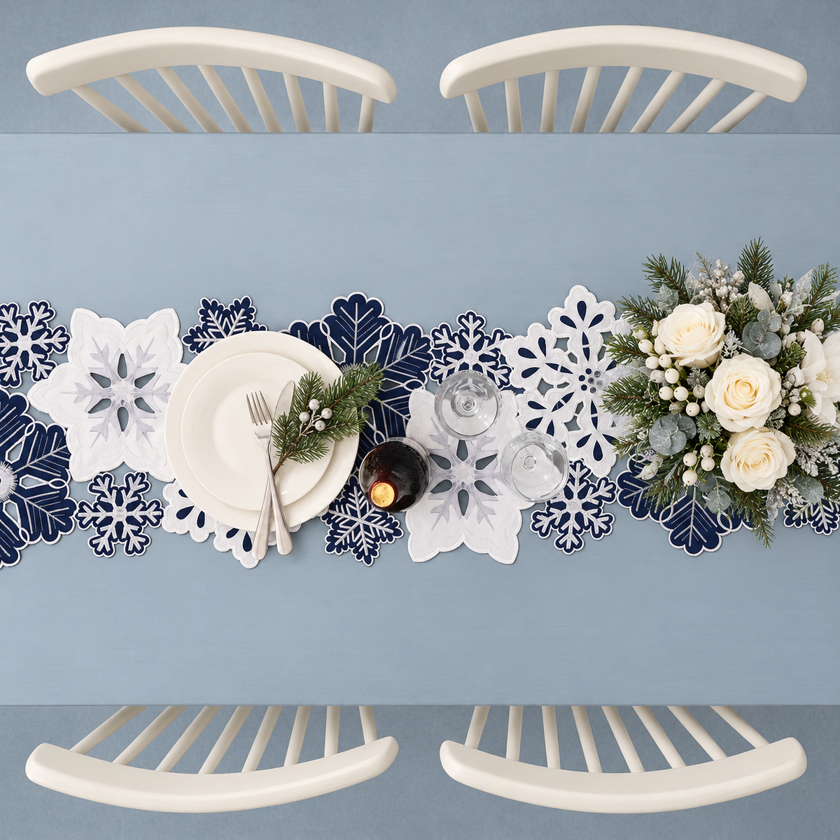 Overhead view of the snowflake cutwork runner with white tableware and winter greenery; styling props not included