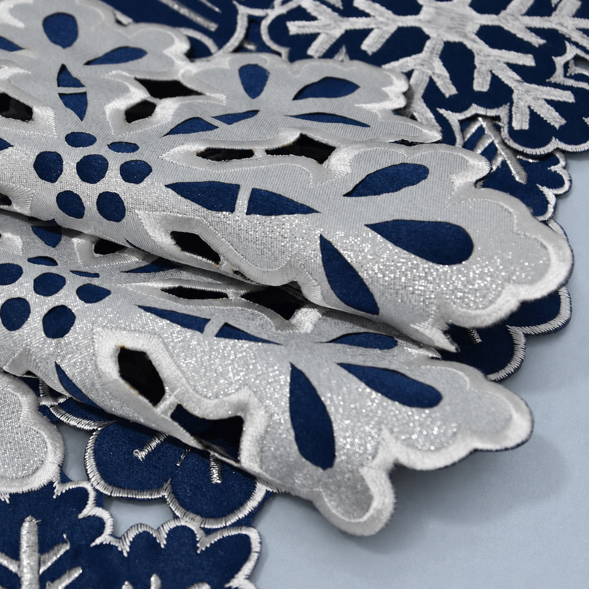 Close-up of folded navy and silver-white fabric, embroidery and cutout details of the snowflake runner