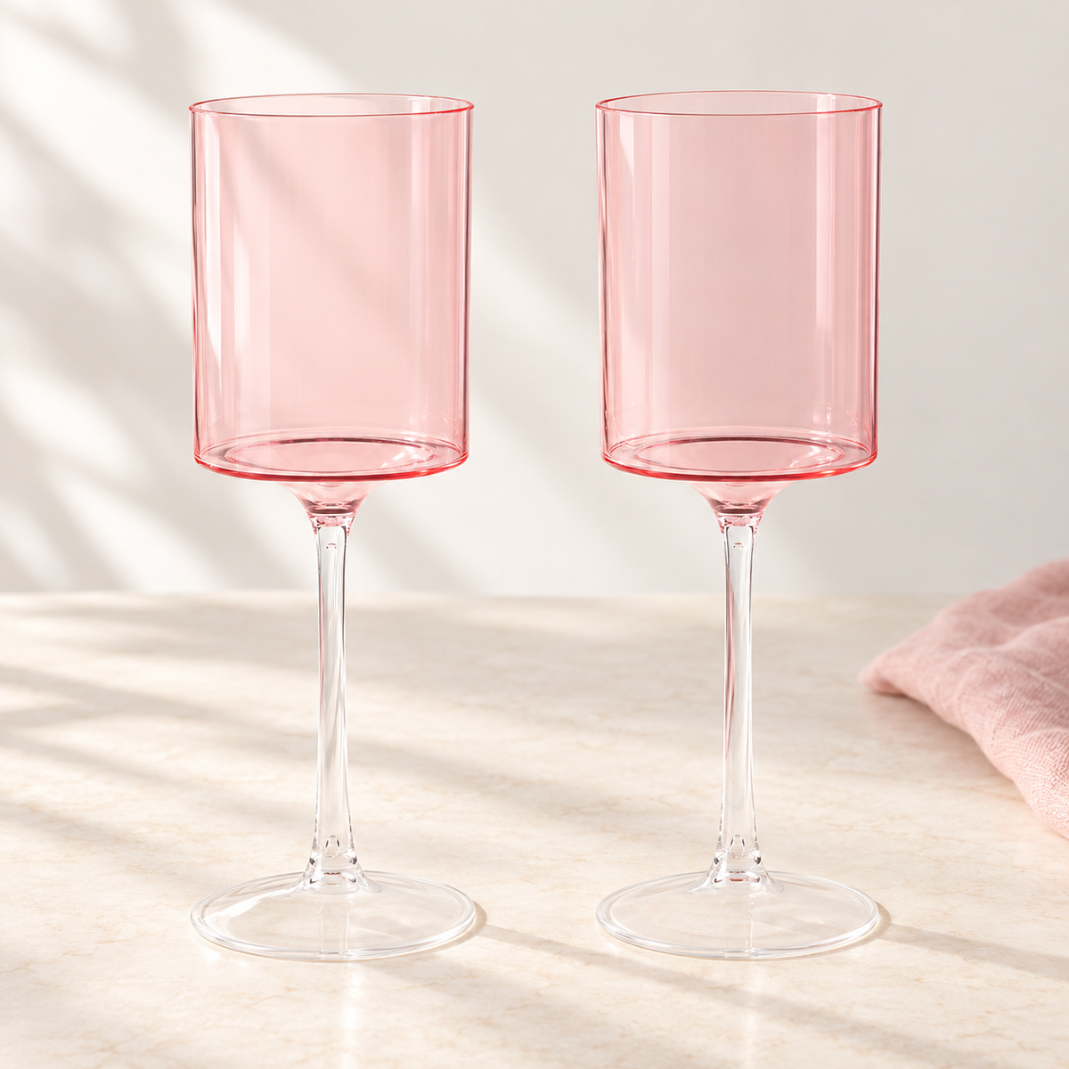 Two pink-and-clear goblets shown separately on a neutral table. Partial arrangement; linen is a styling prop, not included.