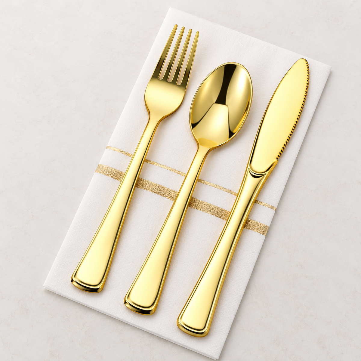 Gold plastic fork, spoon and serrated knife laid on a white and gold pocket napkin. One representative set; pack contains 25 sets.