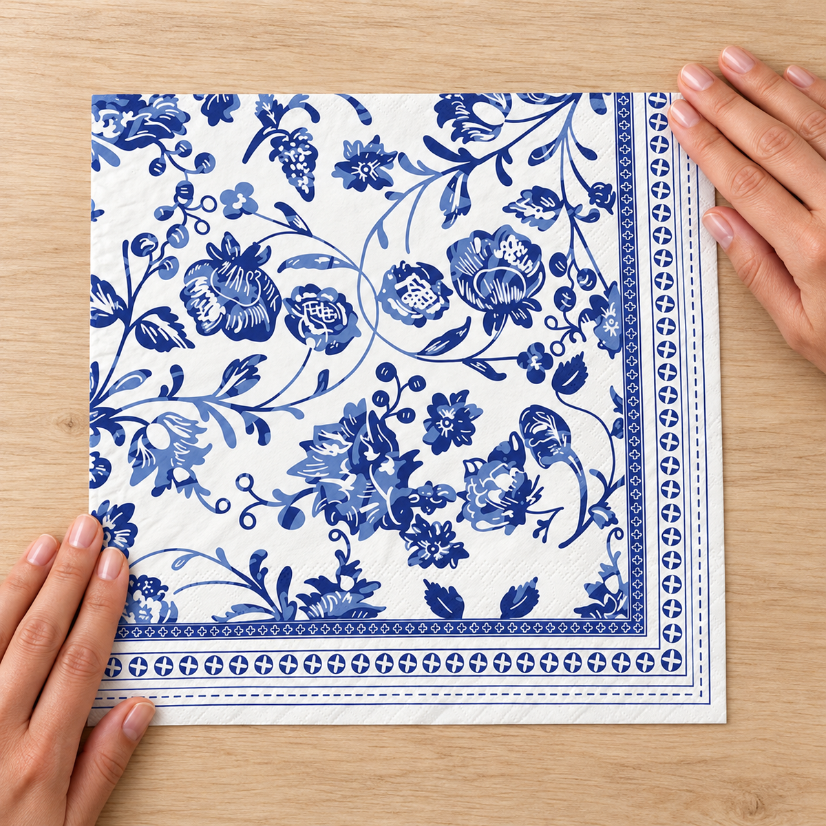 Hands smoothing one folded blue chinoiserie napkin flat, showing its printed square panel