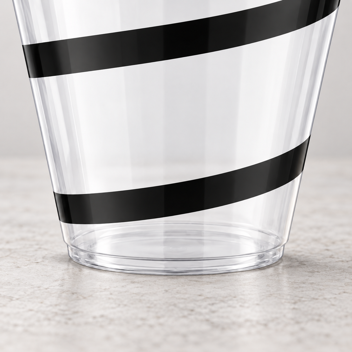 Lower detail of the clear plastic black-swirl cup showing its tapered wall, lower band and flat stemless base.