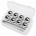 Circular eight-piece whiskey cooling set in its clear storage box with tongs on white.
