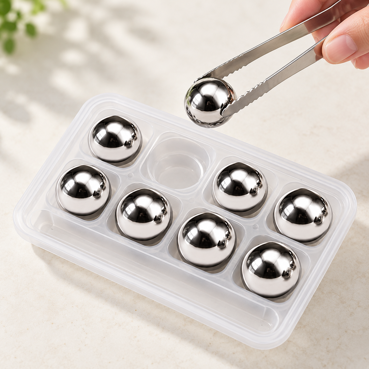 Circular eight-piece whiskey cooling set, with one piece lifted by tongs and seven in the storage tray.