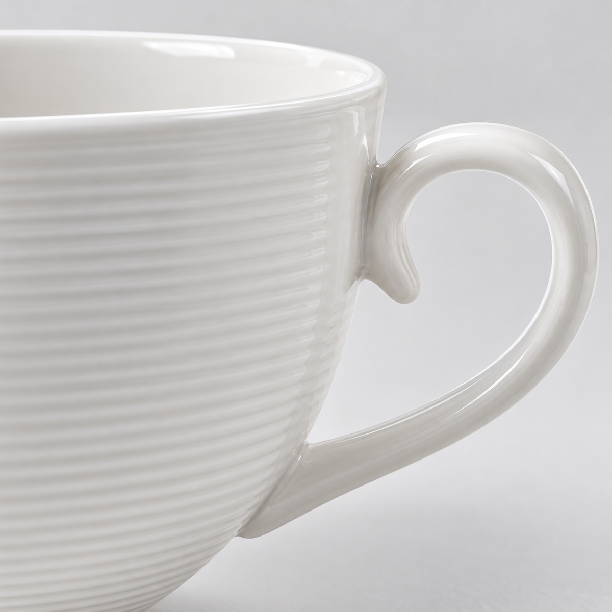Close-up of the fine horizontal ribbing and curled handle of the white ceramic cup.