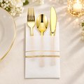 One sample white and gold pocket napkin with gold plastic fork, spoon and serrated knife in a banquet setting. Selling pack contains 25 sets; plates, flowers and candles are not included.