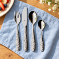 Four-piece WMF Sloth Tommi children's cutlery on blue linen at a family breakfast table; plate, food and flowers are styling props.