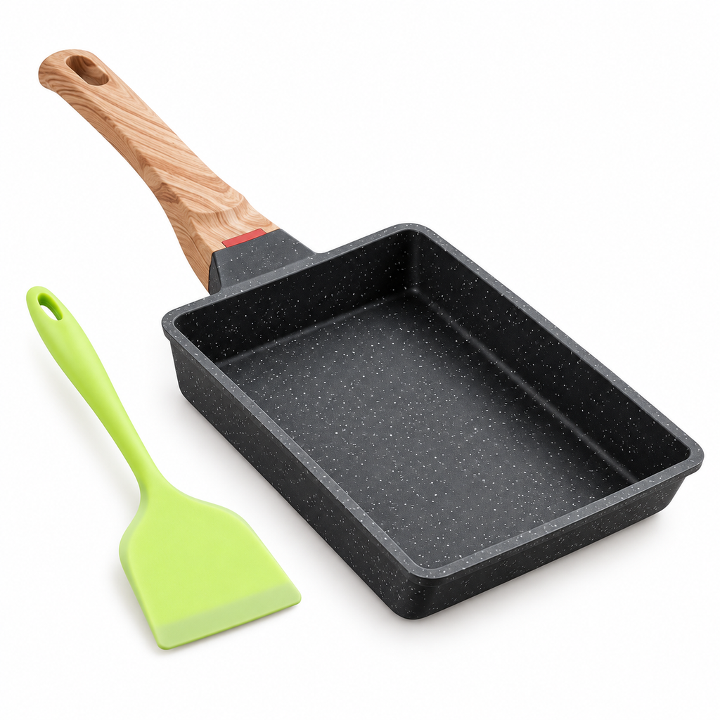 Black speckled tamagoyaki pan with wood-look handle and green spatula on white