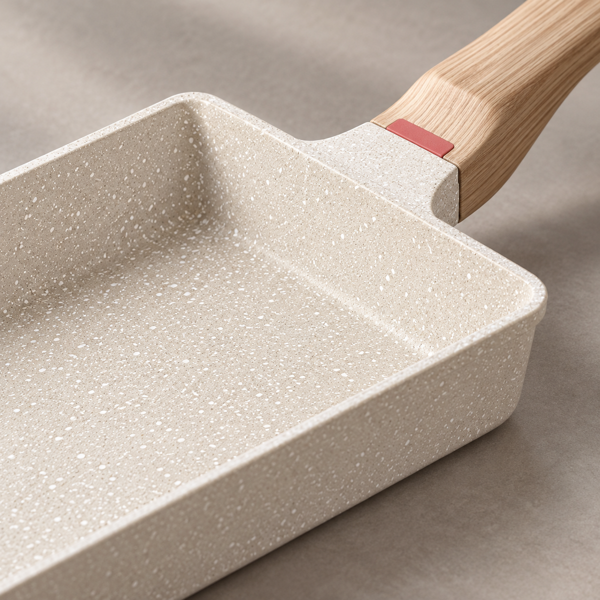 Close-up of white speckled pan surface and wood-look handle connection