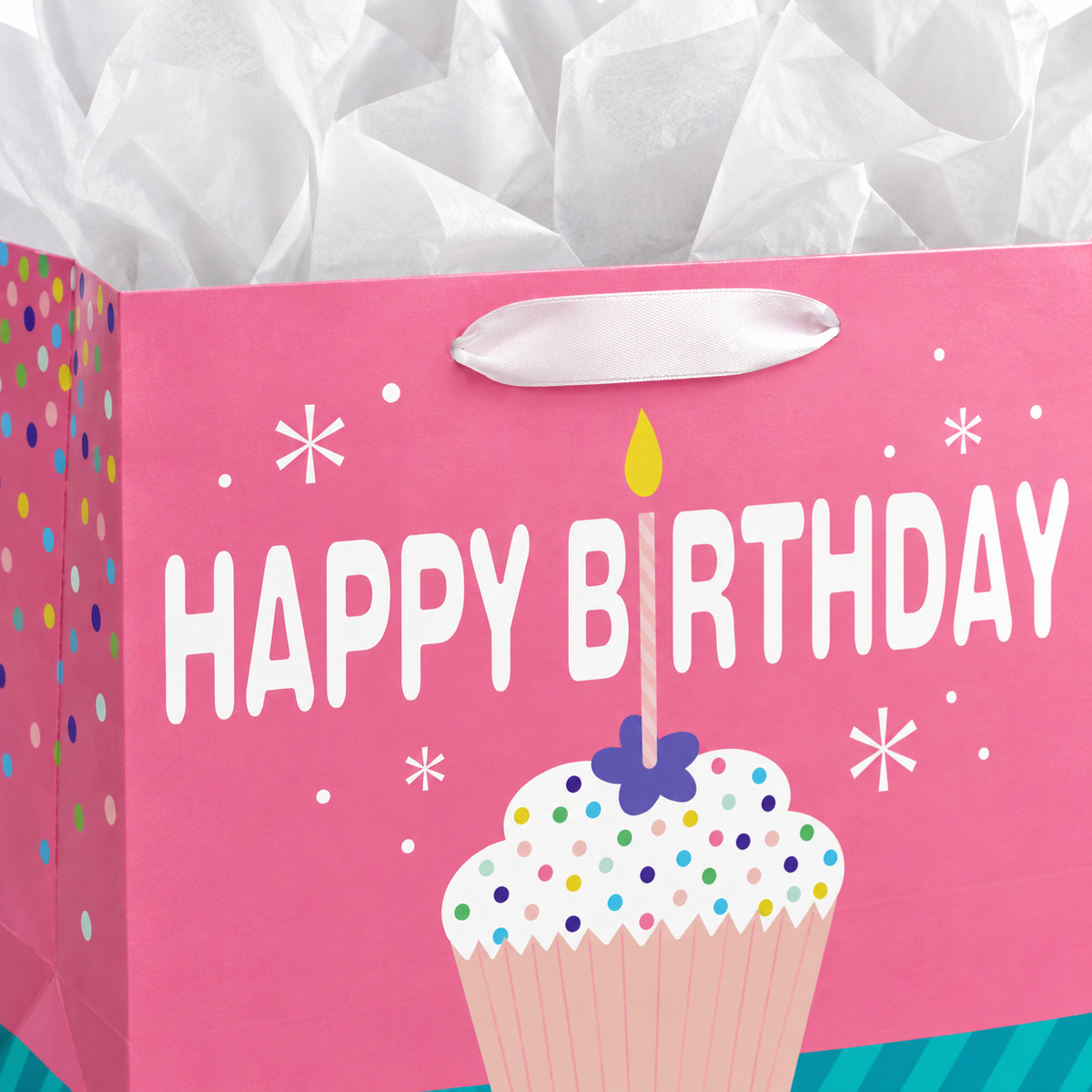Pink cupcake Happy Birthday paper gift bag: print and ribbon handle detail; background objects are styling props