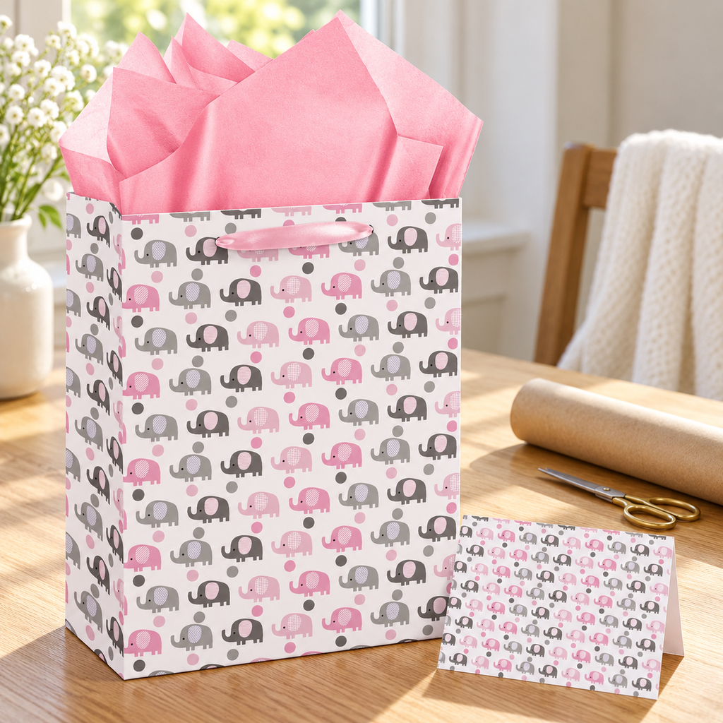 Pink elephant gift bag, pink tissue and matching card on a gift-wrapping desk; tools are styling props