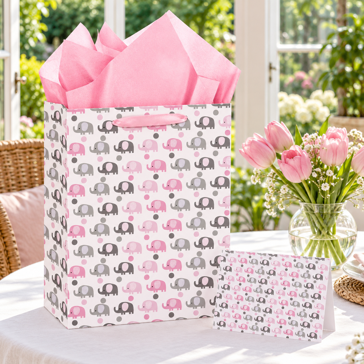 Pink elephant gift bag with tissue and matching card at a conservatory baby shower; flowers are styling props